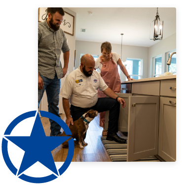 Plumber looking under kitchen sink next to customer and their small dog